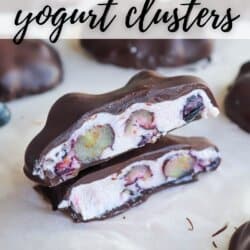 Close-up of two chocolate-covered blueberry yogurt clusters on a parchment paper. One cluster is cut open, revealing blueberries inside creamy yogurt. Text reads Blueberry yogurt clusters at the top and homemadeheather.com at the bottom.