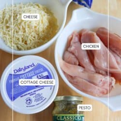 Ingredients on a wooden surface: a bag of spinach, bowls of shredded cheese and raw chicken strips, a container of cottage cheese, and a jar of basil pesto.