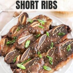 A plate of baked short ribs garnished with sliced green onions and sesame seeds. The text how to bake short ribs is at the top, with homemadeheather.com at the bottom.