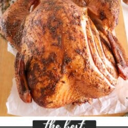 A whole smoked turkey with a crispy, golden-brown skin is displayed on a parchment-lined board. The turkey is seasoned and has a few cuts on its skin. Below, the text reads: the best SMOKED TURKEY homemadeheather.com.