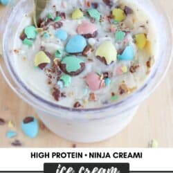 A bowl of Bunny Tracks ice cream is topped with colorful candy pieces and chocolate bits. A gold spoon lies in the bowl. Text on the image reads: High Protein Ninja Creami Ice Cream, homemadeheather.com. Multicolored candies are scattered around.