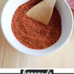 A white bowl filled with red homemade hamburger seasoning is on a wooden surface. A wooden spoon rests in the bowl. A red and white striped cloth is partially visible in the background. Text at the bottom reads, Homemade Hamburger Seasoning.