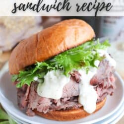 A roast beef sandwich on a plate with lettuce and creamy sauce, served on a glazed bun. The background includes a blurred out ingredient or condiment container. Text on the image reads: Roast Beef Sandwich Recipe and homemadeheather.com.