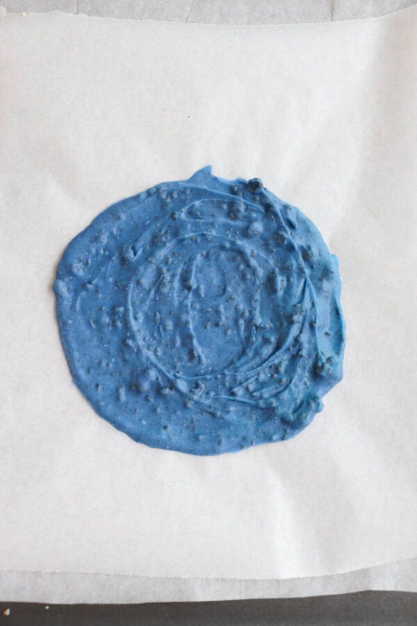 Blue chocolate spread on a piece of parchment paper, with a slightly uneven circular shape and small bubbles visible in the texture.