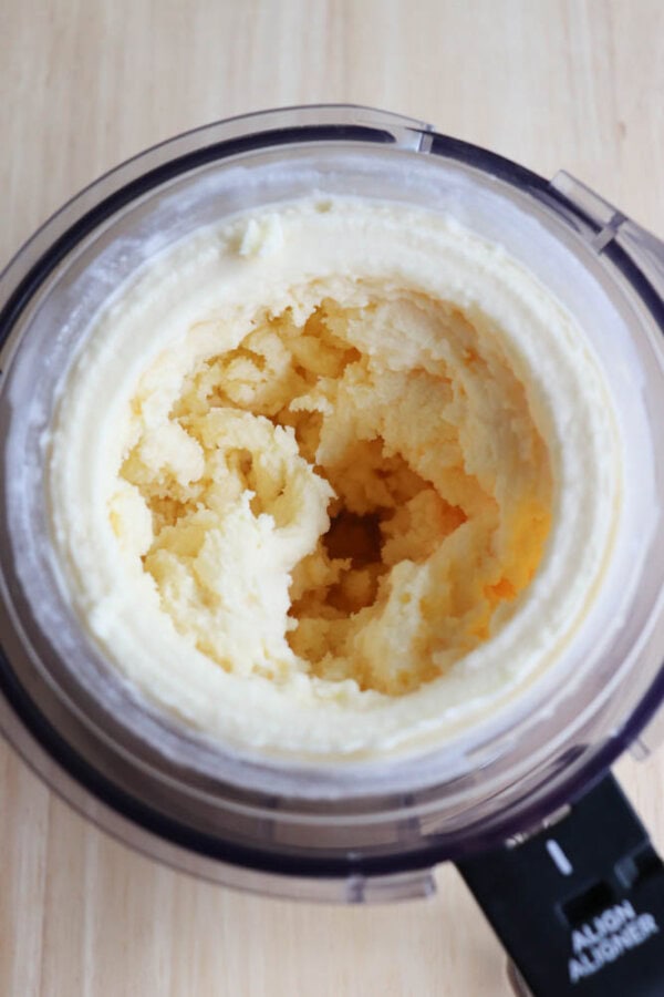 A close-up of creamy, whipped mashed potatoes inside a clear mixing bowl, set on a light wooden surface. The texture appears smooth and fluffy, with a slightly uneven surface.