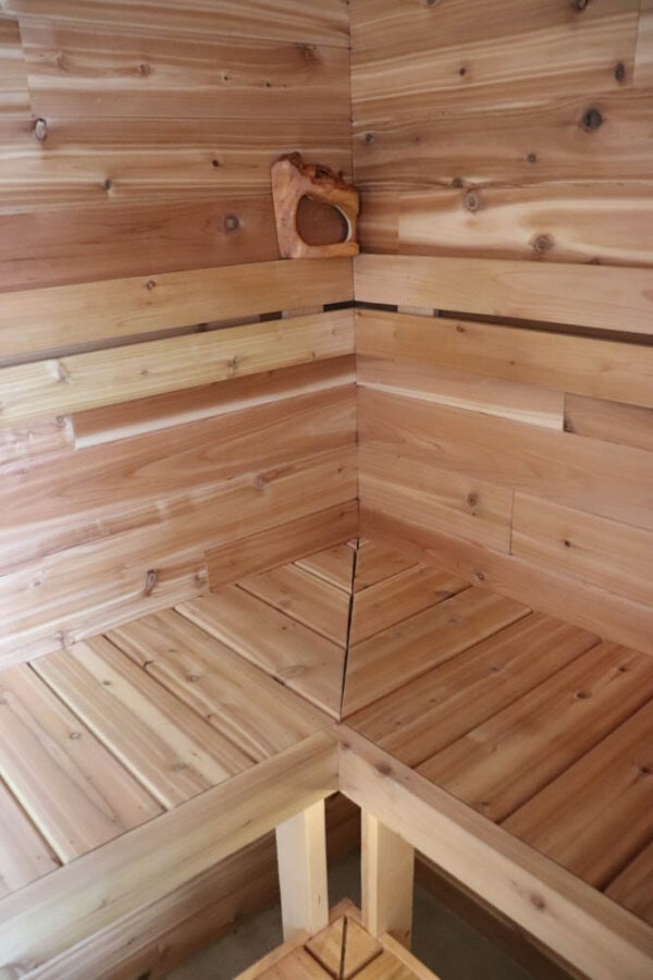 A corner of a wooden sauna with smooth, natural wood paneling and benches. An abstract wooden sculpture rests on the top bench. The space is empty, warm, and inviting with soft lighting highlighting the wood grains.