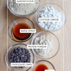 Overhead view of five clear bowls featuring ingredients for cottage cheese protein balls: almond flour, cottage cheese, maple syrup, protein powder, chocolate chips, and vanilla. The labeled bowls are neatly arranged on a wooden surface.