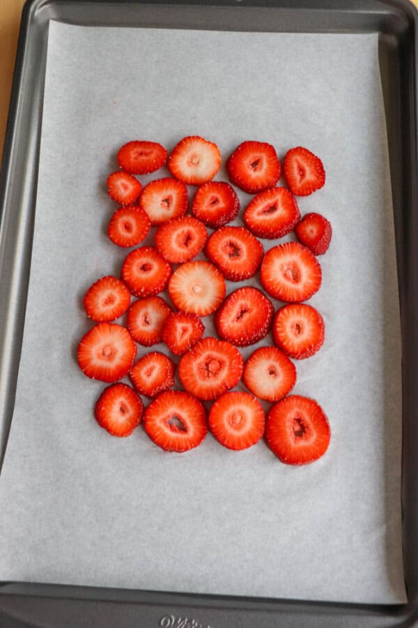 Sliced strawberries arranged in a grid pattern on a baking sheet lined with parchment paper. The strawberries are red and evenly spaced.