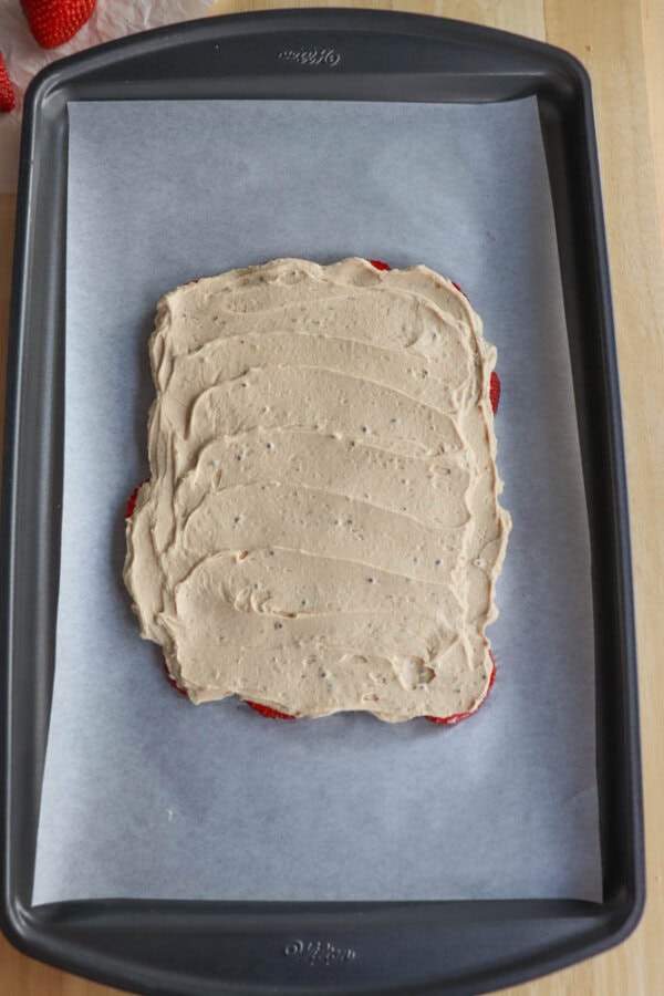 A rectangular layer of strawberries with a layer of peanut butter filling spread evenly on top, placed on a parchment-lined baking tray.