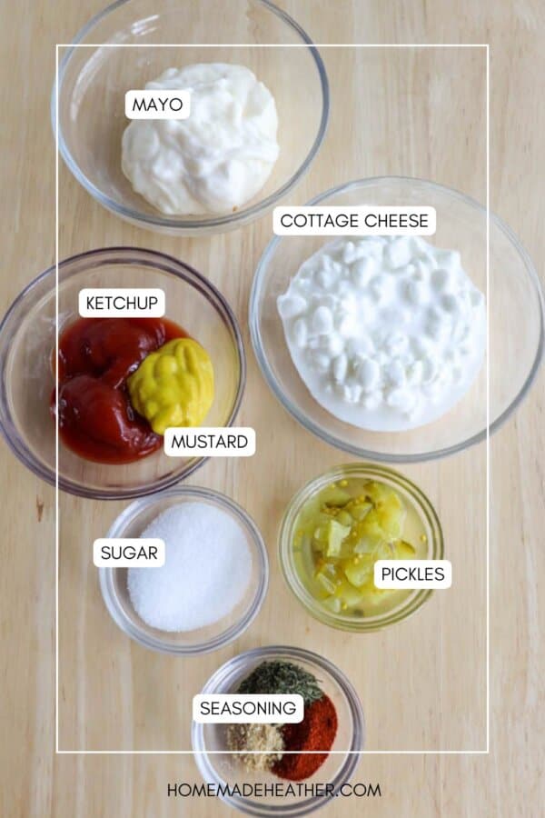 Top-down view of ingredients for a recipe on a wooden surface. Includes bowls of mayo, cottage cheese, ketchup, mustard, pickles, sugar, and seasoning, each labeled.