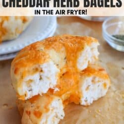 Three cottage cheese cheddar herb bagels on a sheet of parchment paper, with one bagel torn in half showing a textured inside. Text overlay reads Cottage Cheese Cheddar Herb Bagels in the Air Fryer!.