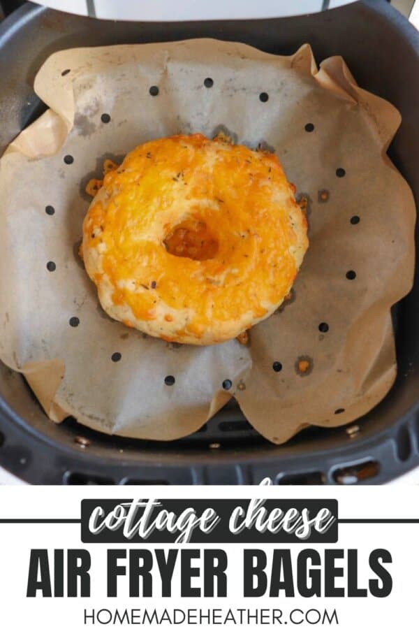 A cottage cheese bagel with melted cheese on top sits on parchment paper inside an air fryer basket. The image also includes text that reads cottage cheese air fryer bagels and homemadeheather.com.