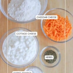Top-down view of labeled ingredients in bowls on a wooden surface: gluten-free flour, cheddar cheese, cottage cheese, herbs, and baking powder.