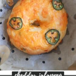 A cheddar jalapeno Greek yogurt bagel on parchment paper. The bagel is topped with melted cheddar cheese and jalapeno slices. Text at the bottom reads cheddar jalapeno Greek yogurt bagels homemadeheather.com.