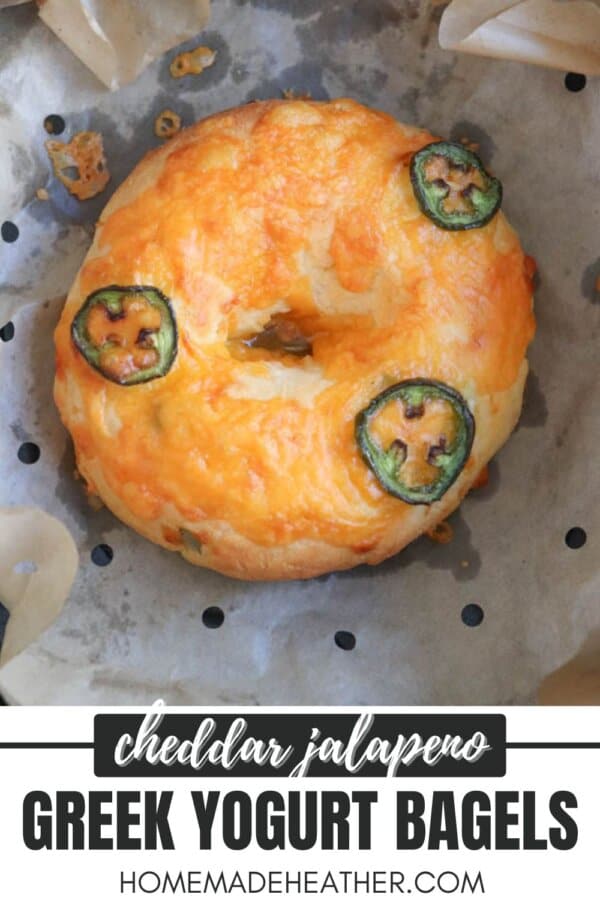 A cheddar jalapeno Greek yogurt bagel on parchment paper. The bagel is topped with melted cheddar cheese and jalapeno slices. Text at the bottom reads cheddar jalapeno Greek yogurt bagels homemadeheather.com.