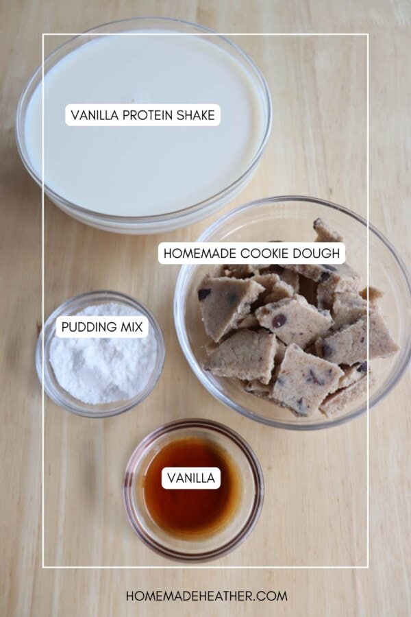 A top view of four labeled glass bowls on a wooden surface. They contain vanilla protein shake, homemade cookie dough, pudding mix, and vanilla. Labels describe each ingredient.