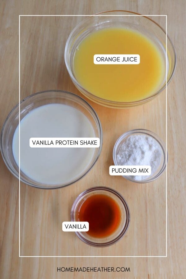Bowls on a wooden surface hold the secret to a refreshing copycat Orange Julius recipe, with ingredients labeled: orange juice, vanilla protein shake, pudding mix, and vanilla extract.