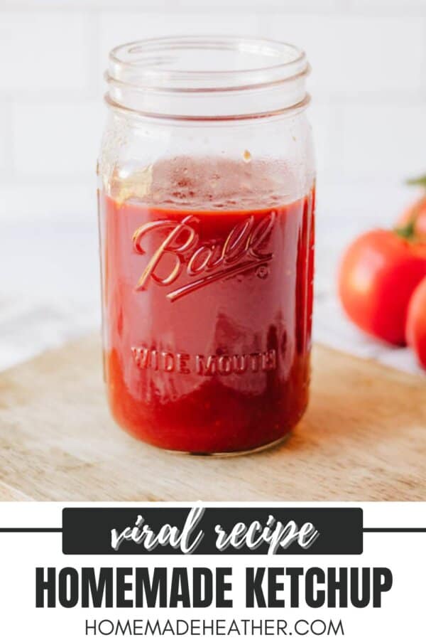 A glass jar filled with homemade ketchup sits on a wooden surface. The jar is labeled Ball and Wide Mouth. Two tomatoes are in the background. Text at the bottom reads: Viral Recipe - Homemade Ketchup - HomemadeHeather.com.