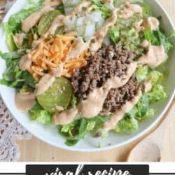 A bowl of Big Mac salad on a lace placemat, topped with ground beef, chopped onions, pickles, shredded cheese, and drizzled with creamy dressing. Text overlay reads: Viral Recipe Big Mac Salad homemadeonheather.com.
