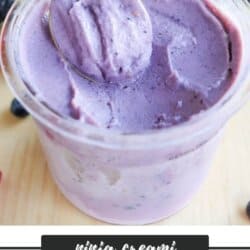 A spoon is dipped into a creamy, purple bumble berry ice cream in a clear container. Mixed berries are scattered around. The text reads ninja creami, bumble berry ice cream, homemadeheather.com at the bottom.