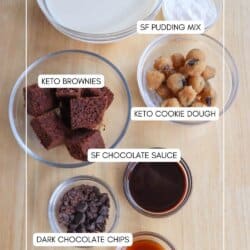 A wooden table displays various labeled ingredients in bowls: protein shake, SF pudding mix, keto brownies, keto cookie dough, SF chocolate sauce, dark chocolate chips, and vanilla. Text says HOMEMADEHEATHER.COM.
