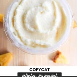 A creamy, light yellow dessert in a bowl sits on a wooden surface, surrounded by small pineapple chunks. Text overlay reads Copycat Ninja Creami Dole Whip and homemadeheather.com.