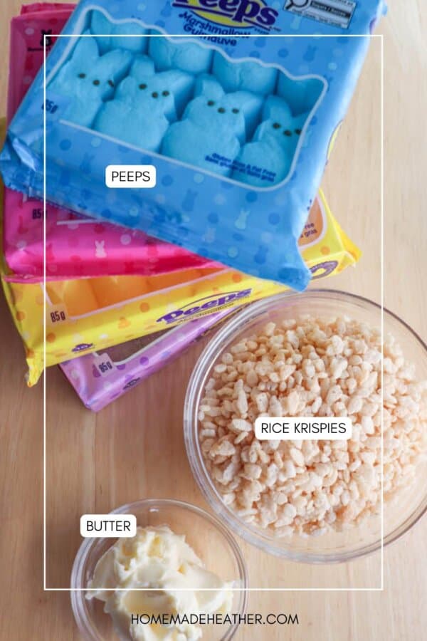Packages of Peeps in yellow, pink, and blue are stacked beside a bowl of Rice Krispies and a small bowl of butter on a wooden surface.