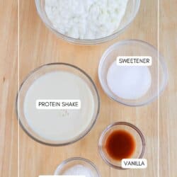 Top-down view of ingredients in bowls on a wooden surface. Labeled: cottage cheese, sweetener, protein shake, vanilla, and SF pudding mix. Website: homemadeheather.com.