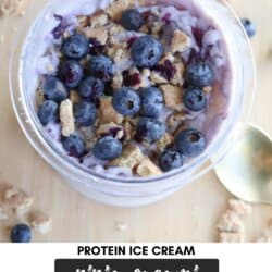 A bowl of blueberry cheesecake ice cream protein-packed and topped with fresh blueberries and crumbled biscuits. A spoon sits beside the bowl. Text reads: Protein Ice Cream Ninja Creami Blueberry Cheesecake homemadeheather.com.