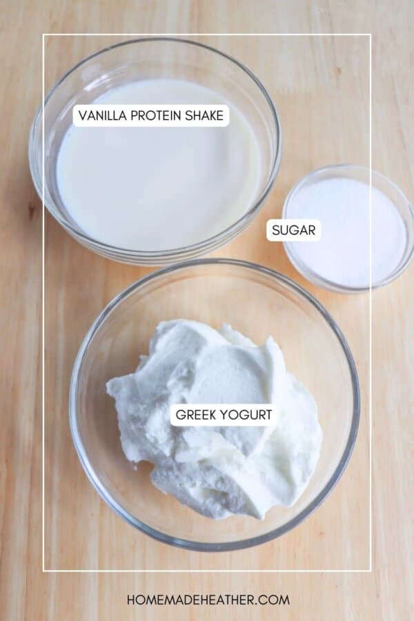 Three glass bowls on a wooden surface: one with vanilla protein shake, another with sugar, and the last with Greek yogurt. Each bowl is labeled accordingly.
