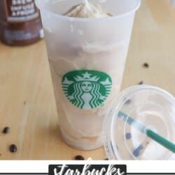 A Starbucks cup filled with a blended coffee drink sits on a table. The lid is off to the side, with coffee beans scattered nearby. In the background, there is a Starbucks bottle labeled Cold Brew Coffee Concentrate. Text reads Starbucks Frappuccino Recipe.