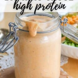 A jar of high-protein Big Mac sauce is open, with some sauce dripping from the rim onto a spoon. The background features a salad and a fork. Text overlay says, BIG MAC SAUCE high protein.