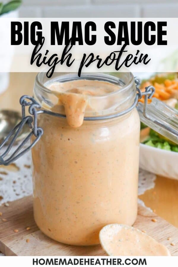 A jar of high-protein Big Mac sauce is open, with some sauce dripping from the rim onto a spoon. The background features a salad and a fork. Text overlay says, BIG MAC SAUCE high protein.