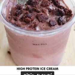 A cup of high protein ice cream with brownie chunks on top, alongside a spoon. The label on the image says Ninja Creami Two Bite Brownie and Homemade Heather. The container is filled to the Max Fill line.
