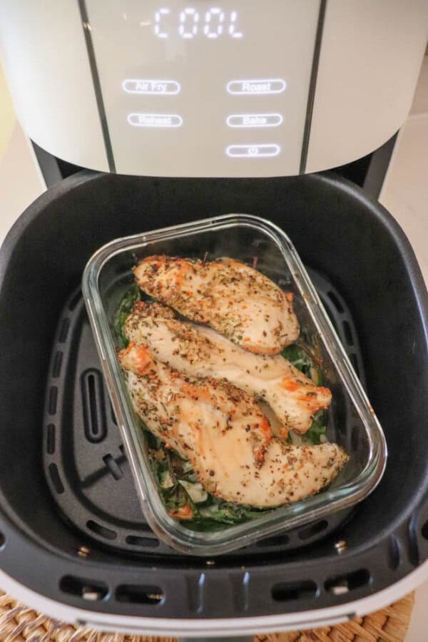 Chicken breasts seasoned with herbs nestle alongside a rich pesto in a glass dish inside an air fryer. The display reads COOL, with handy buttons for air fry and roast functions, creating a seamless cooking experience.