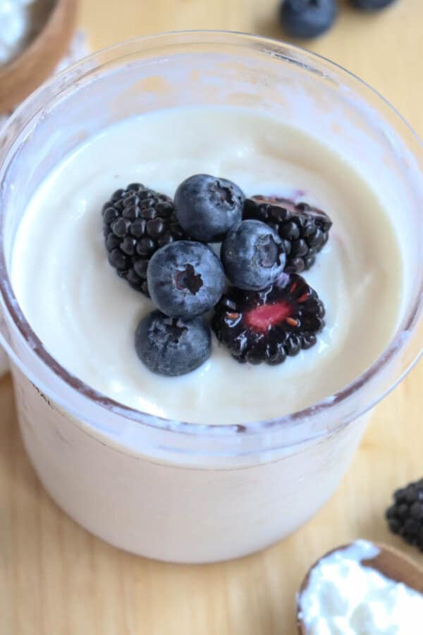 A jar of creamy cottage cheese ice cream topped with fresh blueberries and blackberries, placed on a wooden surface.