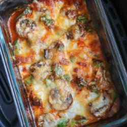 A deliciously baked cottage cheese dish with melted cheese, mushrooms, and green peppers in a clear rectangular glass container. Placed in a black air fryer basket, the top layer is golden-brown with bubbling cheese reminiscent of pizza bowls.