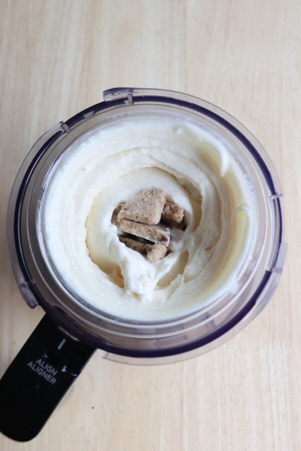 A ninja creami creamy white ice cream with chunks of cookie dough visible in the center, placed on a light wooden surface.