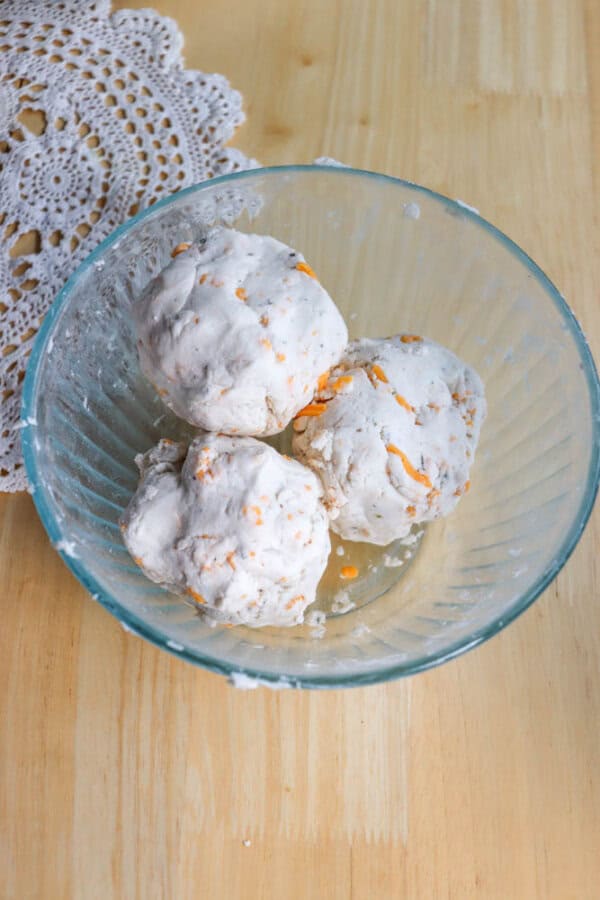 Three dough balls in a glass bowl on a wooden table, with a lace doily partially visible in the background.