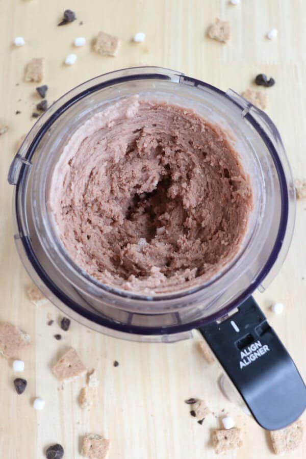 Top view of a ninja foodie containing blended chocolate dessert mixture. The surrounding wooden surface is scattered with chocolate chips, mini marshmallows, and pieces of graham crackers.