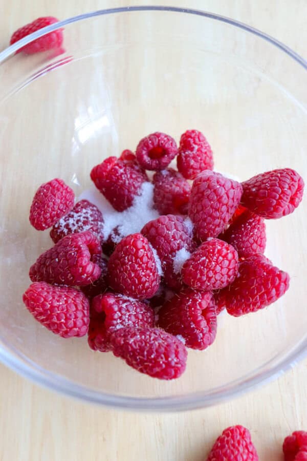 Raspberries in a clear glass bowl with sugar.