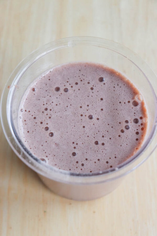 A plastic pint filled with a frothy, brown smoothie, reminiscent of a copycat Wendys Frosty, rests on a light wooden surface.