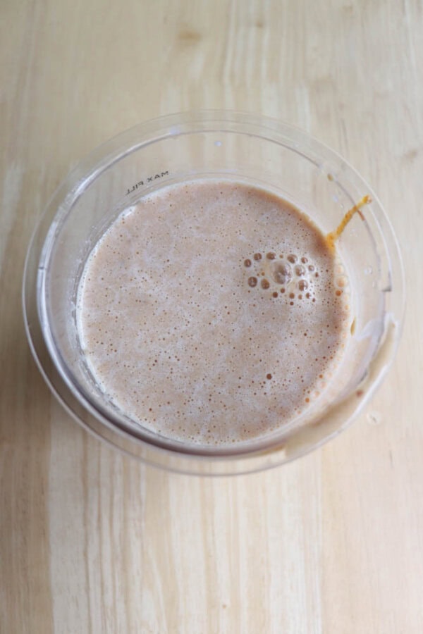 A plastic container filled with a frothy, pumpkin mixture, on a wooden surface. Bubbles are visible on the surface of the drink.