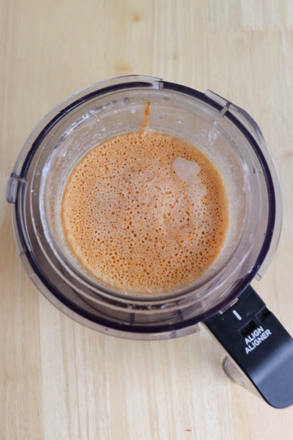 A ninja creami cup viewed from above contains a frothy orange mixture. Its placed on a light wooden surface, with part of the lid visible, showing the words ALIGN in white text.