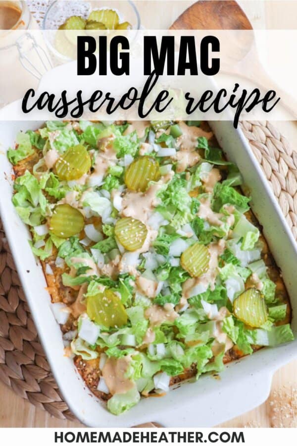 A casserole dish topped with lettuce, pickles, and dressing, resembling a Big Mac. It is surrounded by a woven mat and wooden spoon, with the text “Big Mac casserole recipe” above and “homemadeheather.com” below.