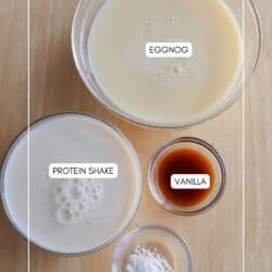 Four bowls on a wooden surface contain eggnog, protein shake, vanilla extract, and pudding mix, each labeled with text inside or near the bowls.