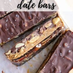 Top view of Snickers-inspired date bars layered with chocolate, nuts, and dates on a parchment. Text overlay reads Snickers Date Bars and homemadeheather.com.