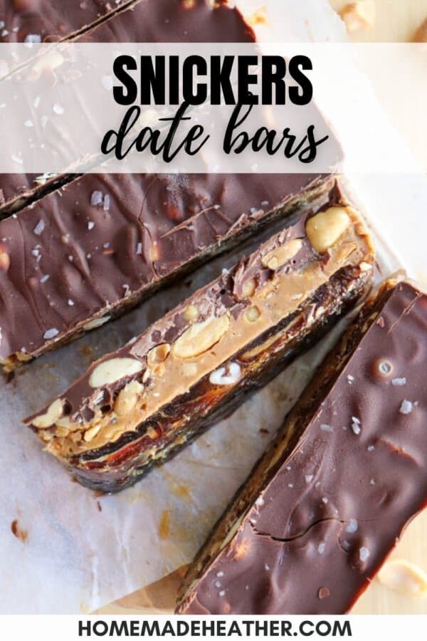 Top view of Snickers-inspired date bars layered with chocolate, nuts, and dates on a parchment. Text overlay reads Snickers Date Bars and homemadeheather.com.