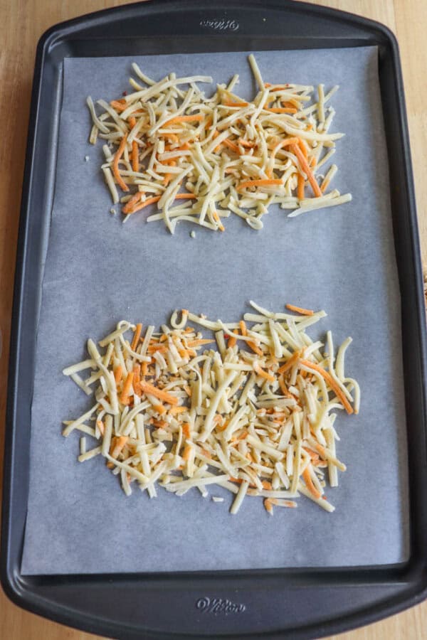 A baking sheet lined with parchment paper holds two separate piles of uncooked shredded potatoes and carrots.