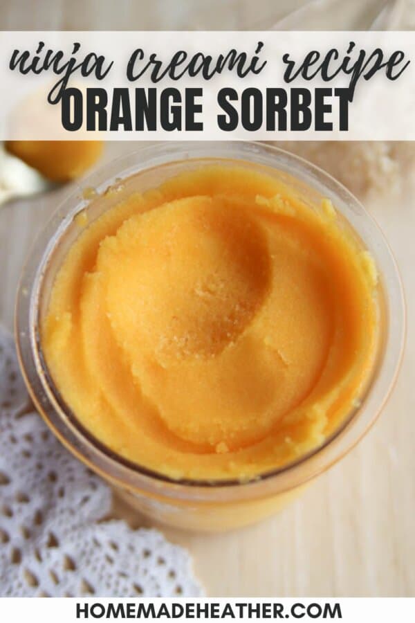 Close-up of a glass container filled with smooth orange sorbet on a light textured surface. A doily is partially visible under the container. Text at the top reads Ninja Creami Recipe and Orange Sorbet. At the bottom is homemadeheather.com.